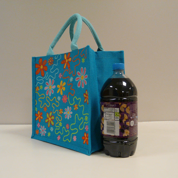 P1110514-Fair-Trade-Jute-Square-Shopping-Bag-Flowers-on-Blue-19704-side-view-with-bottle-of-juice